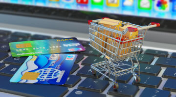 E-commerce, online purchases and internet shopping concept, shopping cart with cardboard boxes and credit cards on laptop keyboard